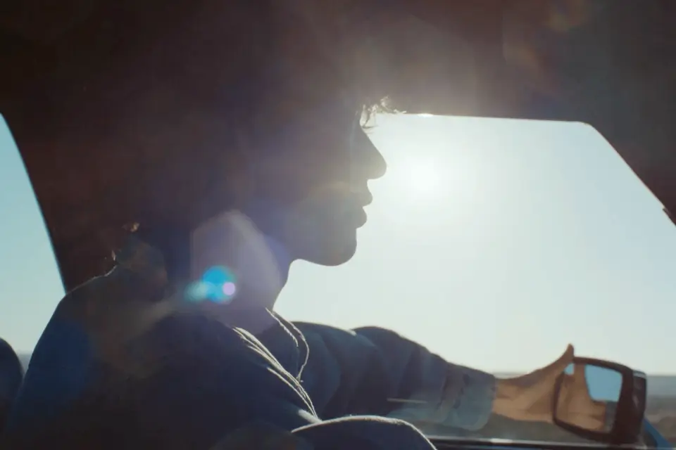 A backlit driver crossing a sunlit desert road
