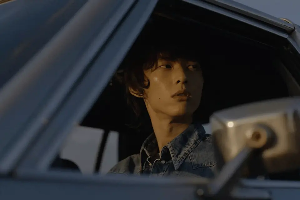 A cinematic portrait framed through the window of a blue car